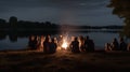 Silhouette of a group of friends sitting around a campfire on the shore of a lake at night