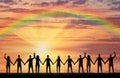 Silhouette of a group of happy people holding hands by the sea at sunset with a rainbow Royalty Free Stock Photo