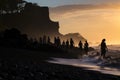 Silhouette of a group of people on the beach at sunset, Silhouettes of tourists enjoying the black sand beach and ocean waves, AI
