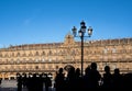 Silhouette of a group of tourists visiting the main square of Salamanca with a wrought iron street lamp illuminated by the midday