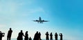 Silhouette of group of unknown people tourists take pictures a landing passenger airplane flying in blue sky background