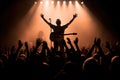 silhouette of a guitarist onstage, audiences hands raised in the air