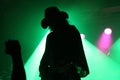 Silhouette of a guitarist on stage with a cowboy hat with fan's fist in front of green reflector