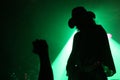 Silhouette of a guitarist on stage with a cowboy hat with fan's fist in front of green reflector