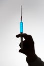 Silhouette of the hand of a doctor with syringe filled with blue liquid. Vaccination concept.