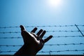 Silhouette hand extending to the sky with barbwire and sunlight