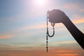 Silhouette of a hand holding Rosary on colorful sunset sky light background. Person with Rosary in hands.