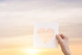 Silhouette of hand is raising paper with shape heart at sunset