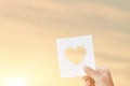 Silhouette of hand is raising paper with shape heart at sunset