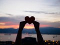 Silhouette hand is raising the red paper heart with blur sunlight during sunset