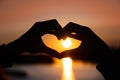 silhouette of hands forming a heart shape with sunset and reflection in the sea Royalty Free Stock Photo