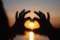 silhouette of hands forming a heart shape with sunset and reflection in the water. Royalty Free Stock Photo