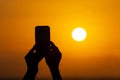 Silhouette of hands holding a mobile phone and making photography of the huge sun during sunset or sunrise Royalty Free Stock Photo