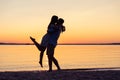 Silhouette of happy couple on beach at sunset, man taking the girl in his arms. Royalty Free Stock Photo