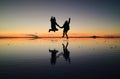 Silhouette of happy couple jumping on the amazing mirror effect of Uyuni Salt Flats against sunset sky, Bolivia, South America Royalty Free Stock Photo