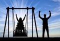 Silhouette of a happy couple, a woman wheelchair user on an adaptive swing and a healthy man nearby