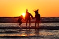 Silhouette of happy friends holding hands and jumping in the water on a coastline at sunset Royalty Free Stock Photo