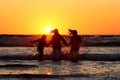 Silhouette of happy friends holding hands and standing in the water on a coastline at sunset Royalty Free Stock Photo