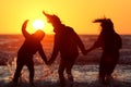 Silhouette of happy friends holding hands and standing in the water on a coastline at sunset Royalty Free Stock Photo