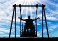 Silhouette of a happy man is a disabled person in a wheelchair on an adaptive swing for disabled people
