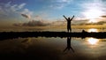 Silhouette of a happy man standing on the beach with his arms wide open showing victory during sunrise morning with reflection.