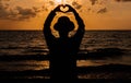 Silhouette of Happy man standing with hands showing heart shape while sunset at sea,Light flare,Enjoys of resting time,Freedom con Royalty Free Stock Photo