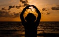 Silhouette of Happy woman standing with hands showing heart shape while sunset at sea,Back view Light flare,Enjoys of resting time Royalty Free Stock Photo