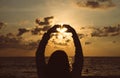 Silhouette of Happy woman standing with hands showing heart shape while sunset at the sea,Back view Light flare,Enjoys of resting Royalty Free Stock Photo