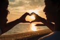 Silhouette of happy young couple forming a heart shape with their hands together on the beach while golden sunset time and sea Royalty Free Stock Photo