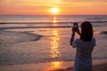 Silhouette of happy young woman taking photo by smartphone.Tourist enjoy beautiful sunset at the beach. Travel, relaxing, vacation Royalty Free Stock Photo