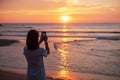 Silhouette of happy young woman taking photo by smartphone.Tourist enjoy beautiful sunset at the beach. Travel, relaxing, vacation Royalty Free Stock Photo