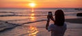 Silhouette of happy young woman taking photo by smartphone.Tourist enjoy beautiful sunset at the beach. Travel, relaxing, vacation Royalty Free Stock Photo