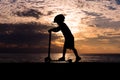 Silhouette of healthy boy riding scooter against background of sea sunset Royalty Free Stock Photo