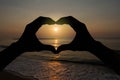 Silhouette heart shaped hands gesturing on blurred sunset over the beach