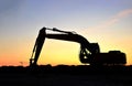 Silhouette of the heavy tracked excavator at a construction site on a background sunset.