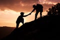 Silhouette of hiker helping each other hike up a mountain at sunset Royalty Free Stock Photo