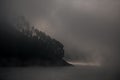 silhouette of a hillside with trees near the water covered with white haze and fog Royalty Free Stock Photo