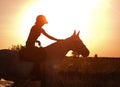 The silhouette of a horse rider patting her horse against the background of sunset Royalty Free Stock Photo