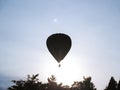 In silhouette hot air balloon drifts through atmosphere above treetops