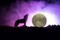 Silhouette of howling wolf against dark toned foggy background and full moon or Wolf in silhouette howling to the full moon. Hallo Royalty Free Stock Photo