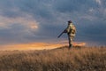 A hunter with a gun in his hands in hunting clothes in the autumn forest in search of a trophy.