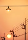 Illuminated hanging street lamp over the road with blurred electric poles against sunset sky background