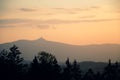 A silhouette of a Jested mountain during sunset with forest in the foreground