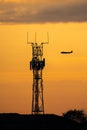 Silhouette jumbo jet flying sunset behind high tech radio mast for communications between pilot and airport. Air traffic control