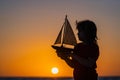 Silhouette of kid playing with toy seailing boat on sunset sea. Little boy playing with toy sailing boat, toy ship Royalty Free Stock Photo