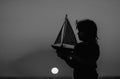 Silhouette of kid playing with toy seailing boat on sunset sea. Little boy playing with toy sailing boat, toy ship Royalty Free Stock Photo