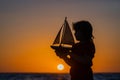 Silhouette of kid playing with toy seailing boat on sunset sea. Little kid boy sailing toy ship on sea water. Summer Royalty Free Stock Photo