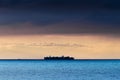 Silhouette of large container ship crossing Baltic sea under dramatic dark nimbostratus cloud formation.