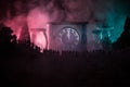 Silhouette of a large crowd of people in forest at night standing against a big arrow clock with toned light beams on foggy backgr