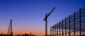 Silhouette of large industrial building structure with pile driver and crane in construction site at sunset